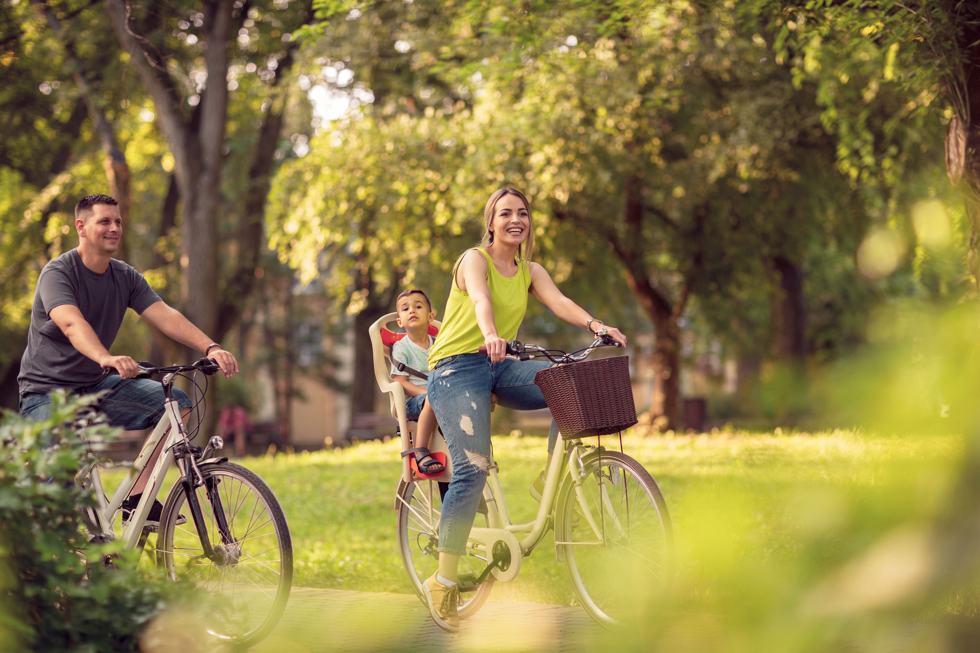 Smiling-father-and-mother-with-kid-on-bicycles-having-fun-in-park_By-Ljiljana